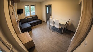 Un espace de vie compact comprenant un canapé, une table à manger et des chaises, un téléviseur et une fenêtre donnant sur un paysage agréable.
