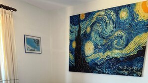 A bedroom with a bed, a nightstand, a wall-mounted painting, and a framed picture. - Villa Pinna (San Teodoro)