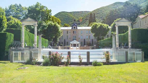 Un bâtiment doté d’un pavillon central, entouré d’un élément aquatique et de verdure.