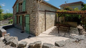 A stone house with green shutters, a tiled patio, and a pergola with vines. - Tranquil Villa in Cévennes (Courry)