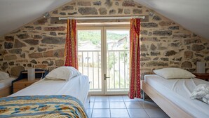 A bedroom with two beds, stone walls, a large window with curtains, and a view of the outside. - Tranquil Villa in Cévennes (Courry)