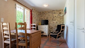 A cozy room with a wooden dining table, chairs, a TV, and a stone wall. - Tranquil Villa in Cévennes (Courry)