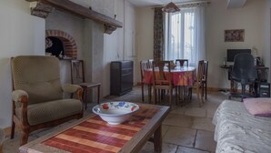 A cozy living room with a fireplace, a dining area with a table and chairs, and a workspace with a computer. - Cottage in an old remote farmhouse (Giroux)