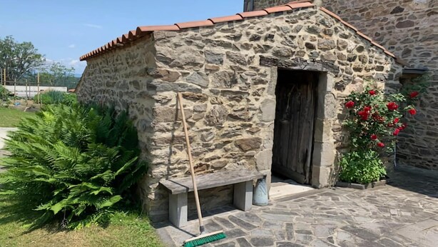 A stone building with a tiled roof, a wooden door, and a bench outside.