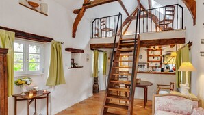 A rustic interior with a wooden staircase, a loft bedroom, and a dining area with a view of the kitchen.