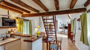 A kitchen with a microwave, wooden beams, a small refrigerator, and a dining area with a chair and table.