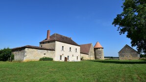 Un bâtiment en pierre doté d’une tour centrale, d’une vaste pelouse et surplombé d’un ciel bleu dégagé.