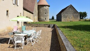 Un bâtiment en pierre doté d’une tour conique, un espace verdoyant avec une table et des chaises, et un petit abri.