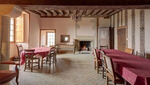 Une salle à manger avec une cheminée, des poutres apparentes et un sol carrelé.