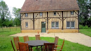 A Tudor-style building with a thatched roof and timber framing, surrounded by a grassy area with a round table and chairs. - Historic Home Saint-Aignan by Lake (Saint-Aignan)