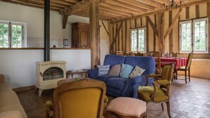 A rustic room with exposed wooden beams, a blue sofa, wooden chairs, a table with a red tablecloth, and a vintage stove. - Historic Home Saint-Aignan by Lake (Saint-Aignan)