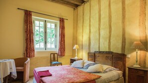 A bedroom with a bed, a chair, a table, and a window with curtains. - Historic Home Saint-Aignan by Lake (Saint-Aignan)