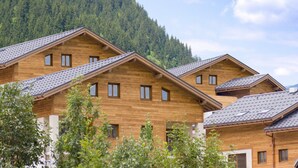 A row of wooden cabins with pitched roofs, set against a backdrop of a forested mountain. - Apartment in Beaufort with Spa Access (Beaufort)