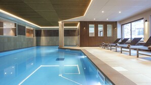 A modern indoor swimming pool with clear water, sun loungers along the side, and large windows providing natural light. - Apartment in Beaufort with Spa Access (Beaufort)