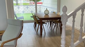 A dining area with a wooden table and chairs, a cushioned chair, and a staircase with white balusters. - Charming 3-bedroom townhome with AC, WiFi in lovely Retamar (Retamar)