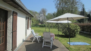 A patio with two white chairs and a table, a large umbrella, and a blue blanket on the ground. - Bungalow in France near Castle & Hiking Trails (Saint Pierre le Vieux)