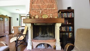 A living room with a brick fireplace, a wooden mantel, and a bookshelf filled with books. - Bungalow in France near Castle & Hiking Trails (Saint Pierre le Vieux)