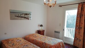 A bedroom with two beds, a chandelier, a painting, a lamp, a radiator, and a balcony with curtains. - Quend-Plage Apartment with Pool (Quend-Plage)