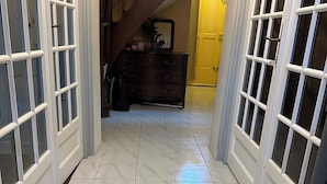 A hallway with white tiled flooring and a wooden staircase. - The bird house (Tours)