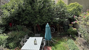 A patio with a table and chairs, surrounded by lush greenery and a garden. - The bird house (Tours)
