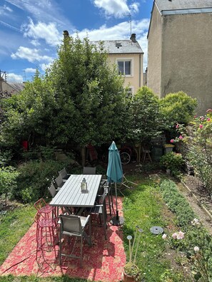 Een terras met een tafel en stoelen, omringd door weelderig groen en een tuin.