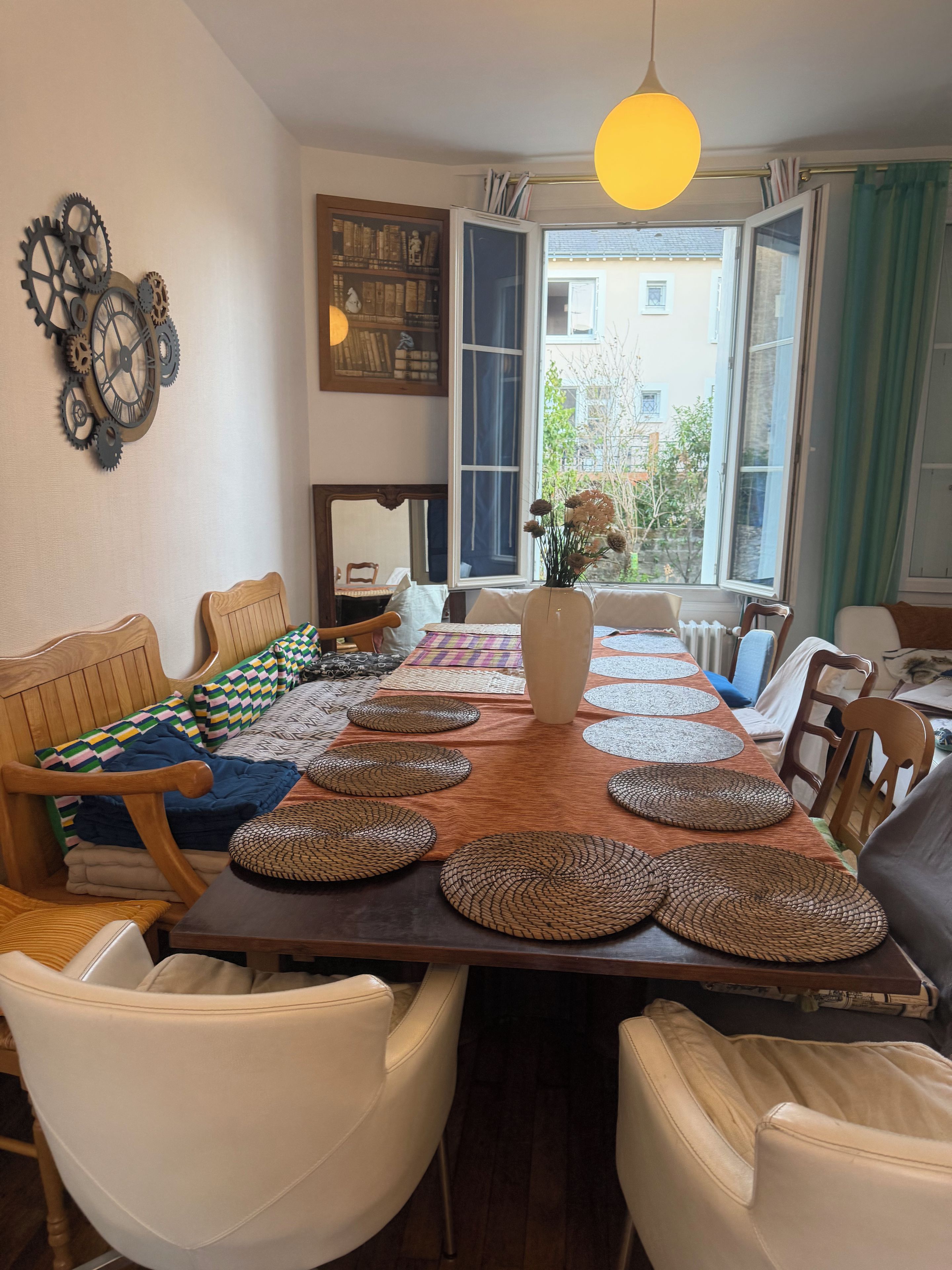 Een eetgedeelte met een lange tafel, stoelen en een uitzicht door open ramen.