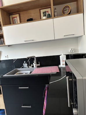 A kitchen with a stainless steel sink, a black countertop, and a white cabinet above.