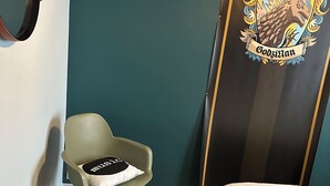 A room with a bed, a green chair, a wooden floor, a round stool, and a door with a coat of arms. - The bird house (Tours)
