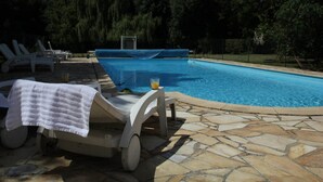 Ein Schwimmbecken mit Liegestühlen und einer überdachten Liegefläche.