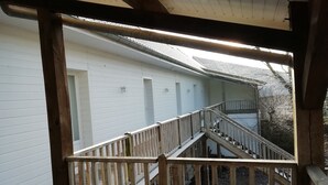 Ein überdachter Außenbereich mit Holzgeländer, einer Treppe, die zu einer unteren Ebene führt, und einem weißen Gebäude im Hintergrund.