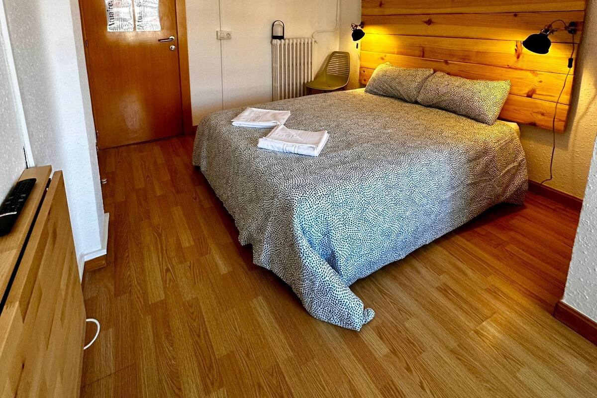 A bedroom with a wooden headboard, a bed with patterned bedding, a bedside lamp, and a radiator.