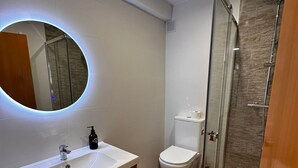A modern bathroom with a white sink, a round mirror, a toilet, and a glass-enclosed shower. - HOSTAL ATUAIREHOME BURGOS (Burgos)