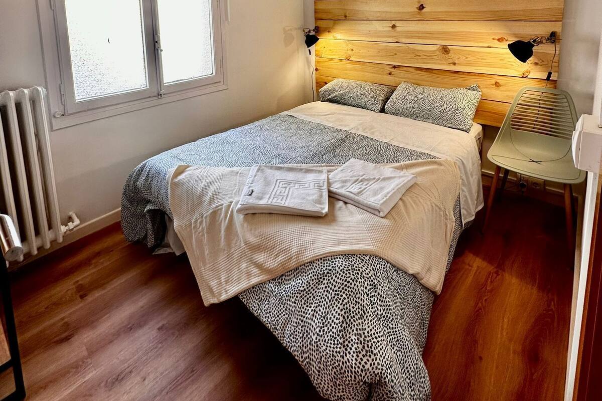 A bedroom with a wooden headboard, a bed with patterned bedding, a radiator, and a window with a blind.