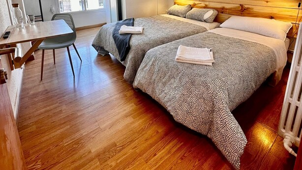 A bedroom with a wooden headboard, two beds with patterned bedding, a desk with a chair, and a hanging light fixture. - HOSTAL ATUAIREHOME BURGOS (Burgos)