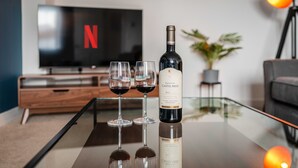 A modern living room with a glass coffee table, two wine glasses, a bottle of wine, a TV displaying the Netflix logo, and a potted plant. - Your Stylish, Spacious 4 Bedroom, 3 Bathroom, home-from-home near all amenities. (Colchester)