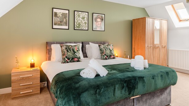 A bedroom with a bed, a nightstand, a wardrobe, and framed botanical prints on the wall. - Your Stylish, Spacious 4 Bedroom, 3 Bathroom, home-from-home near all amenities. (Colchester)