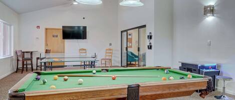 A pool table with balls, a ceiling fan, and a billiard table in a room with a carpeted floor.