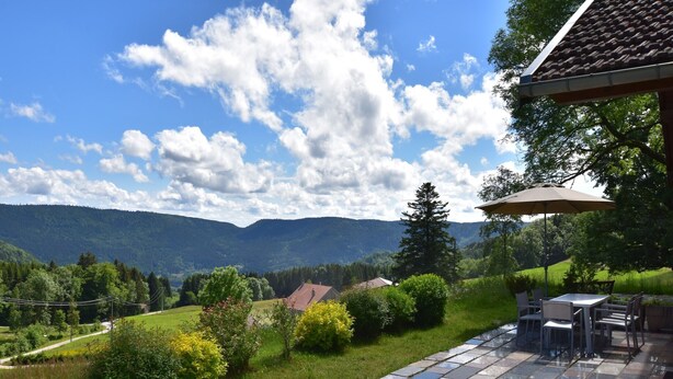 Eine Terrasse mit Steinboden, einem Tisch und Stühlen und Blick auf eine Berglandschaft.