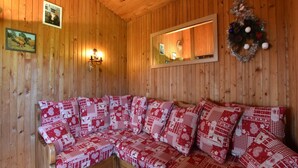 Ein gemütlicher Holzraum mit einer Couch, belegt mit roten und weißen Kissen, einem Wandspiegel und einem Adventskranz mit Dekorationen.