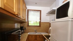 A compact kitchen with wooden cabinets, a built-in oven, a microwave, and a window with a view of the outdoors. - Ventron Chalet with Hill Views (Ventron)