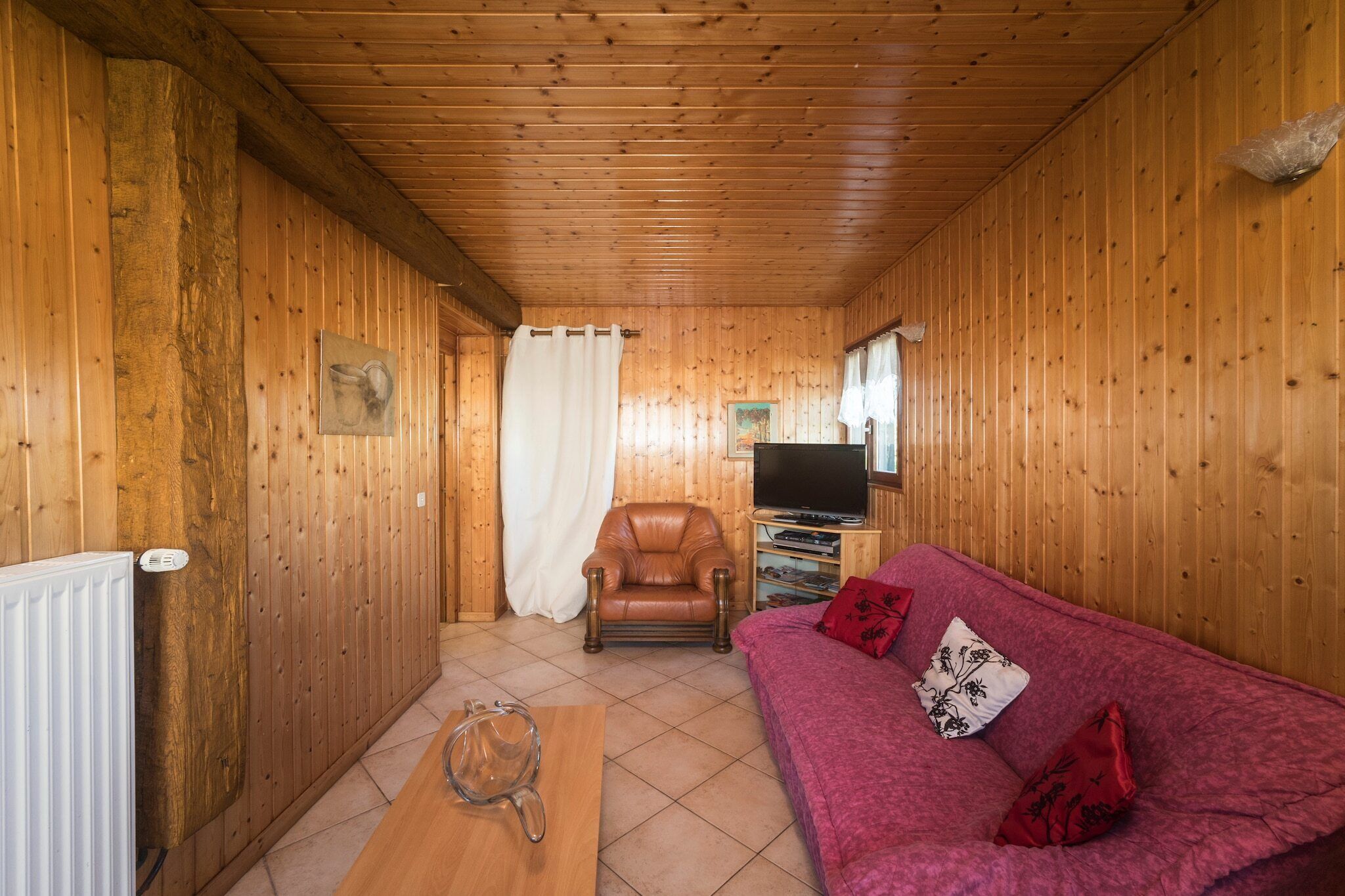 Ein Zimmer mit Holzvertäfelung, einem roten Sofa, einem Ledersessel, einem Fernseher und einer Heizung.