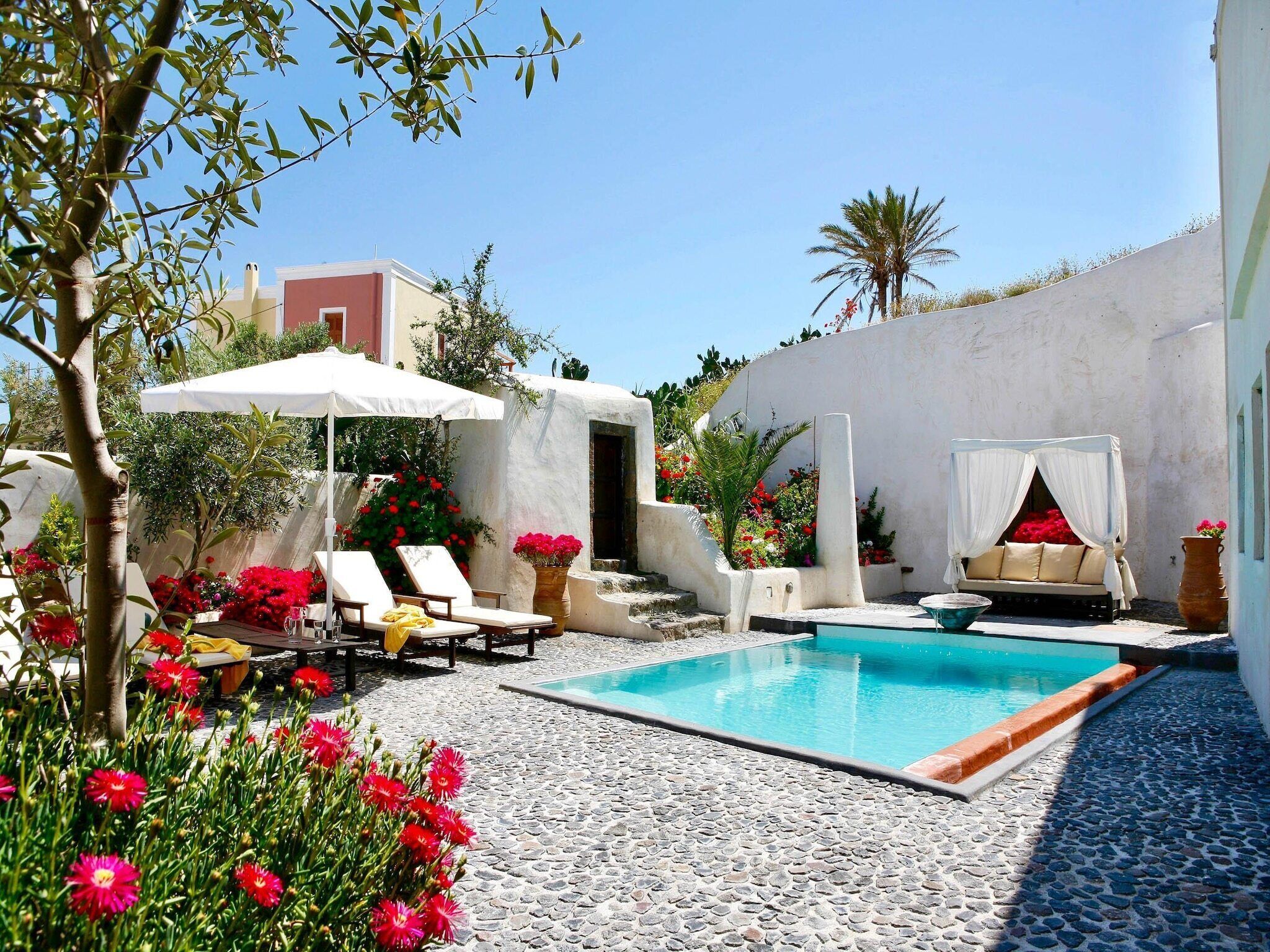 Un espace piscine aménagé avec des chaises longues, un auvent et un petit jardin agrémenté de fleurs rouges.