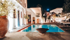 Ein Poolbereich mit Liegestühlen und einem kleinen Pool, umgeben von Topfpflanzen und einem Gebäude mit weißen Wänden.