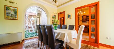 A dining room with a table set for six, a patterned rug, and a view through an arched window.