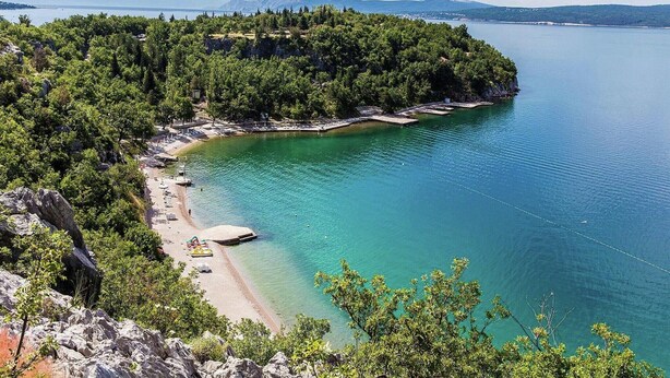 A coastal area with a beach, rocky terrain, and a forested peninsula.