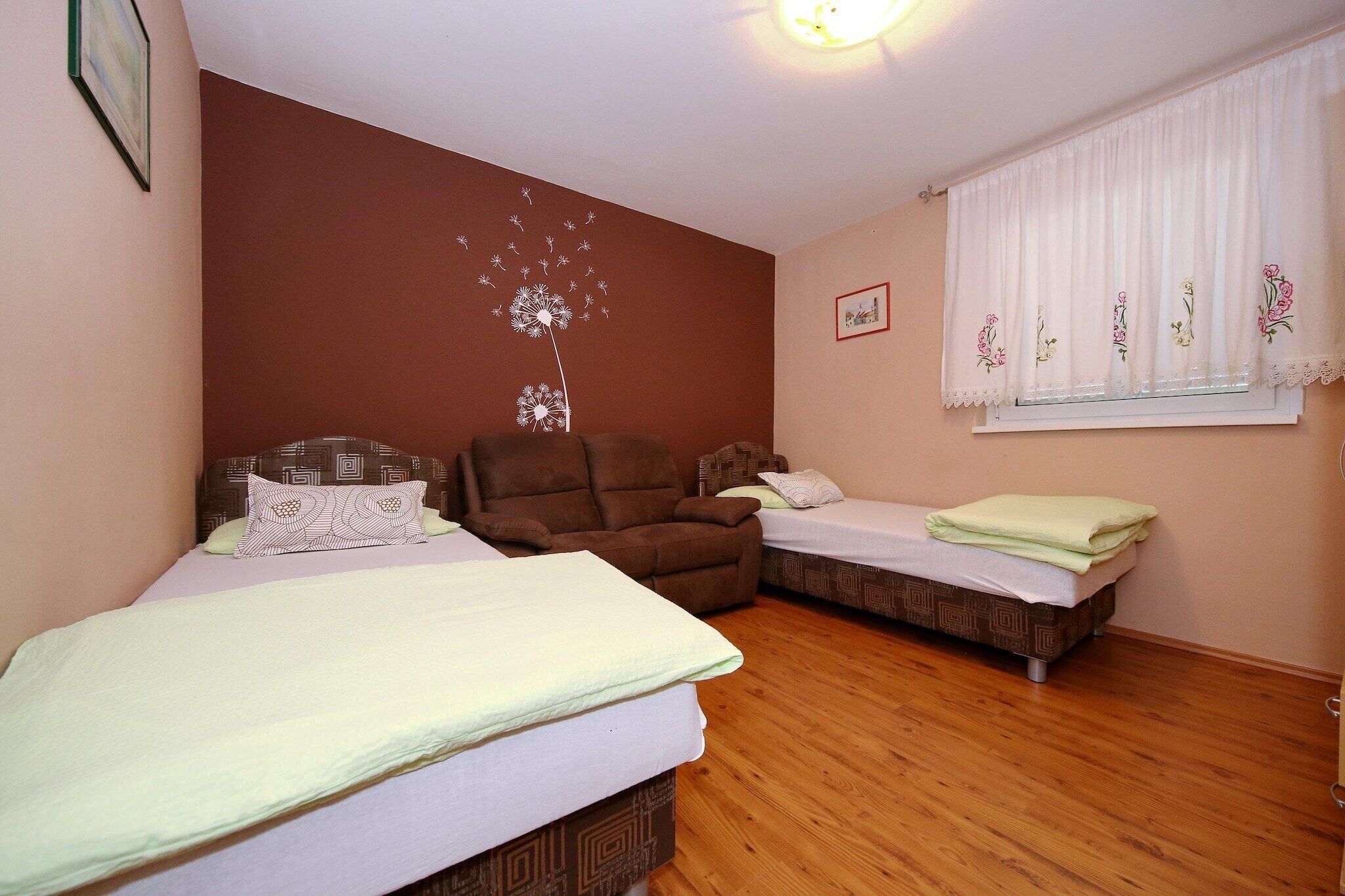 A bedroom with two beds, a brown sofa, a window with floral curtains, and a wall decoration.