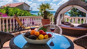 Une terrasse avec des meubles en osier, une table sur laquelle se trouve un saladier rempli de fruits, et une vue sur la mer.