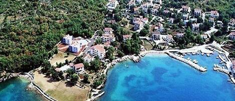 An aerial view of a coastal town with houses, a marina, and clear blue waters.