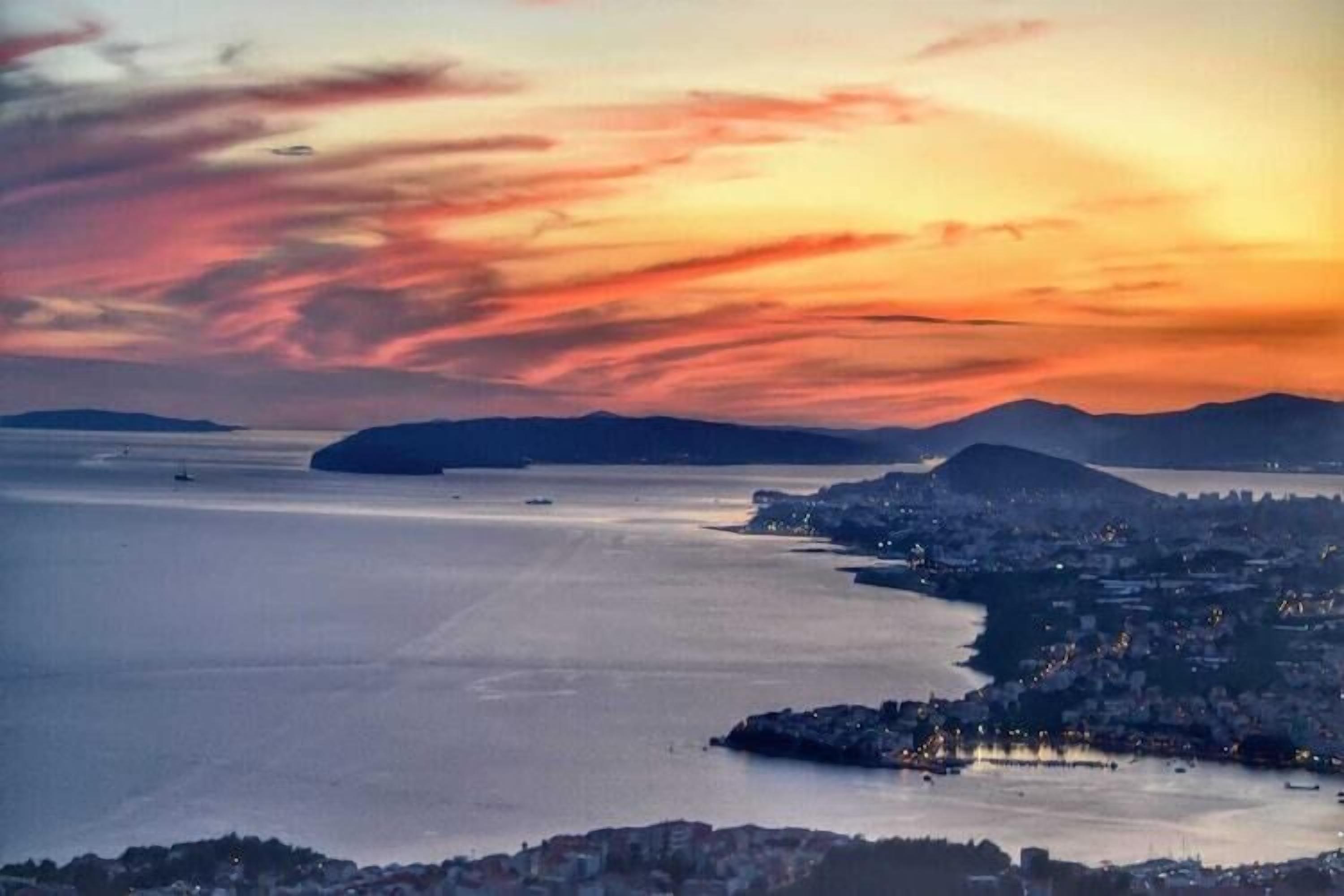 Eine Küstenstadtlandschaft bei Sonnenuntergang mit Blick auf das Meer und ferne Berge.