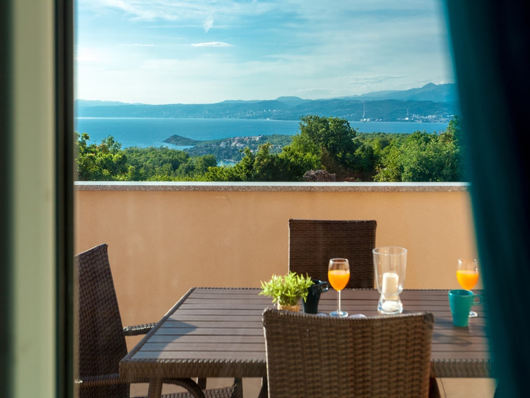 Un balcón con sillas de mimbre y una mesa, con vistas a un paisaje que incluye agua y vegetación.